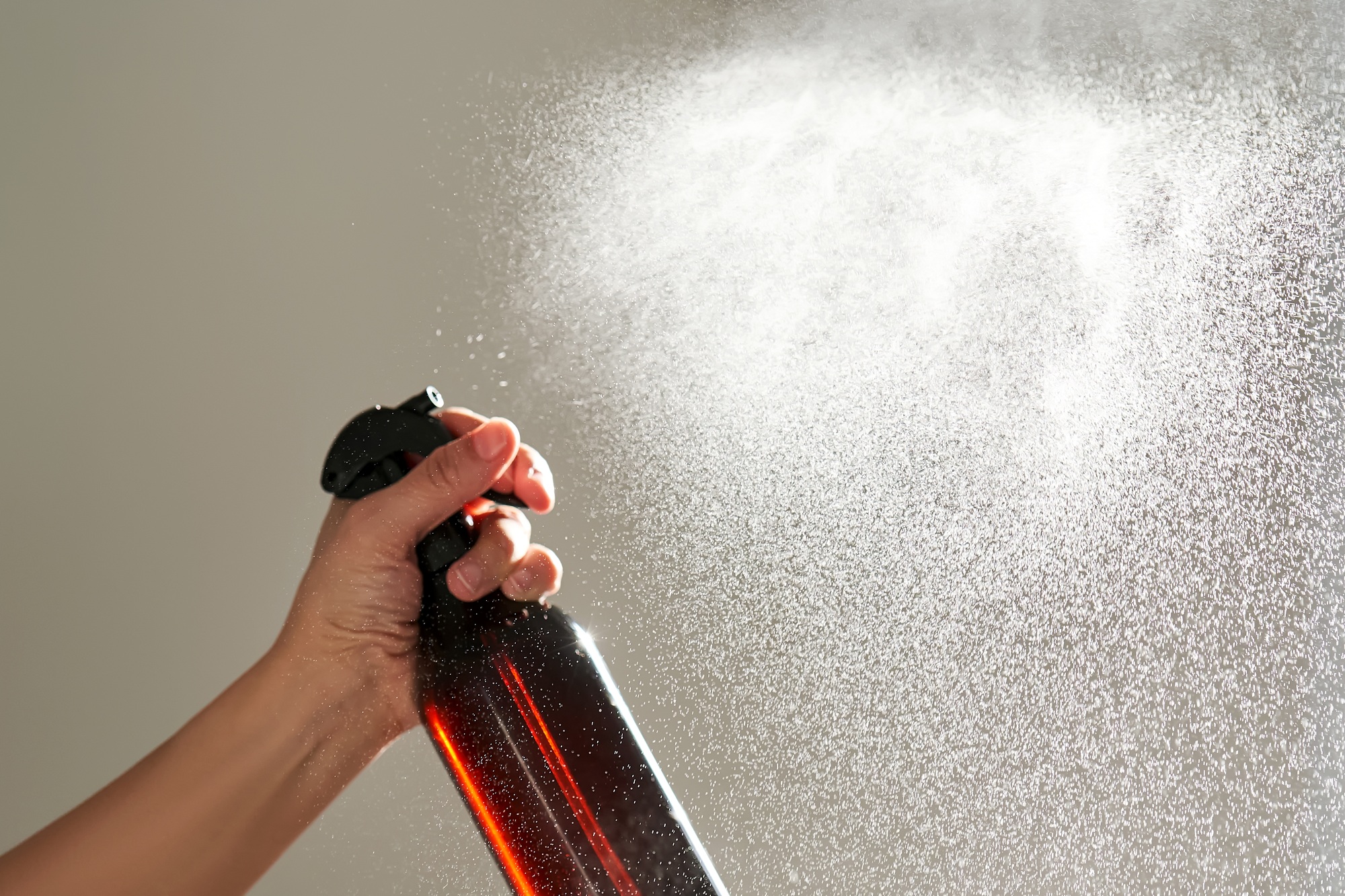 A woman's hand sprays an air freshener in a room.